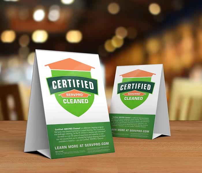 Table tent signs describing the Certified: SERVPRO Cleaned program on top of a wooden table.